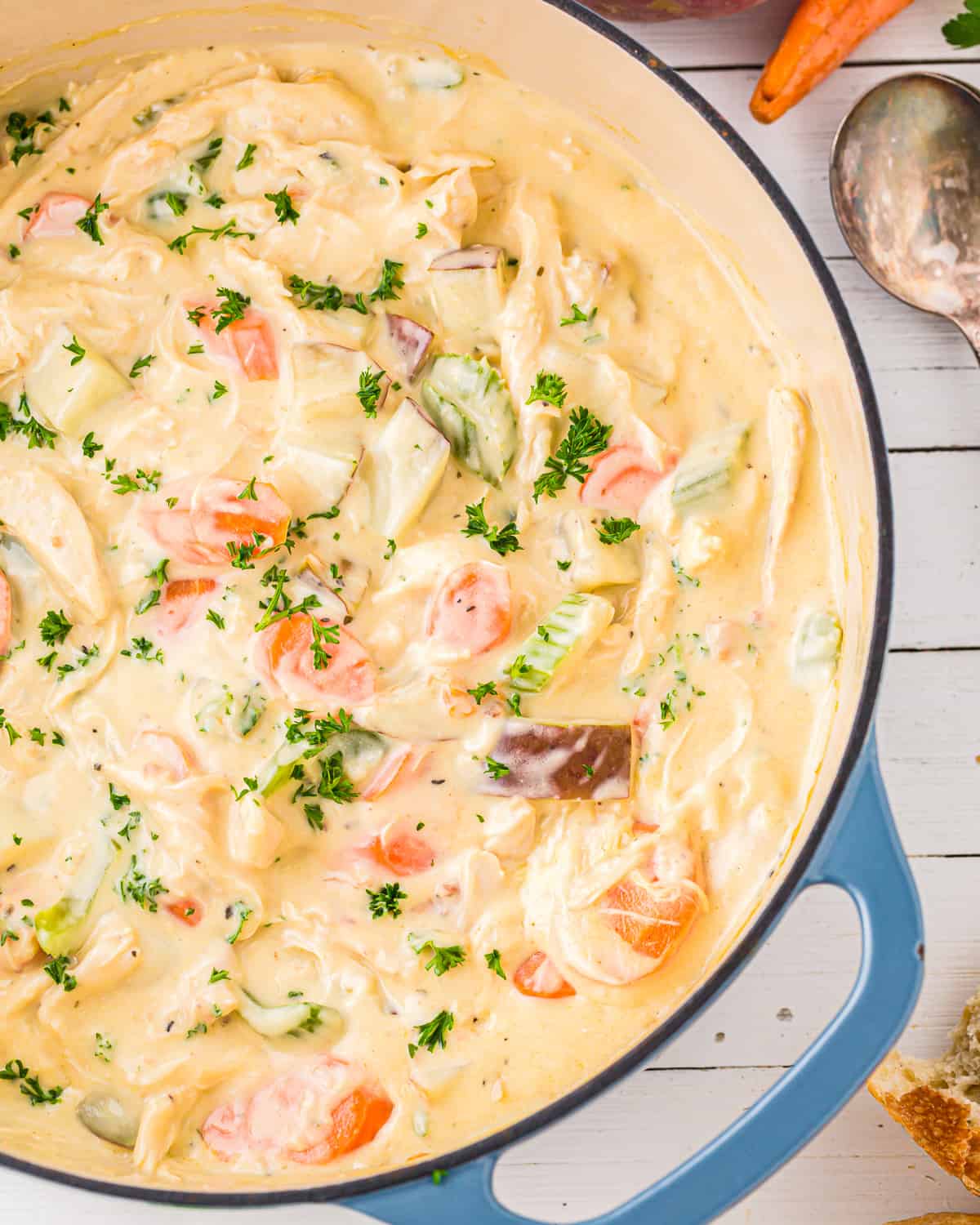 creamy chicken stew in a blue pot with carrots, celery, and potatoes.