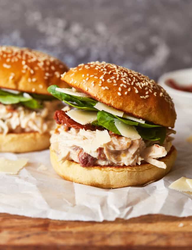 side view of 2 chicken alfredo sandwiches on parchment paper.