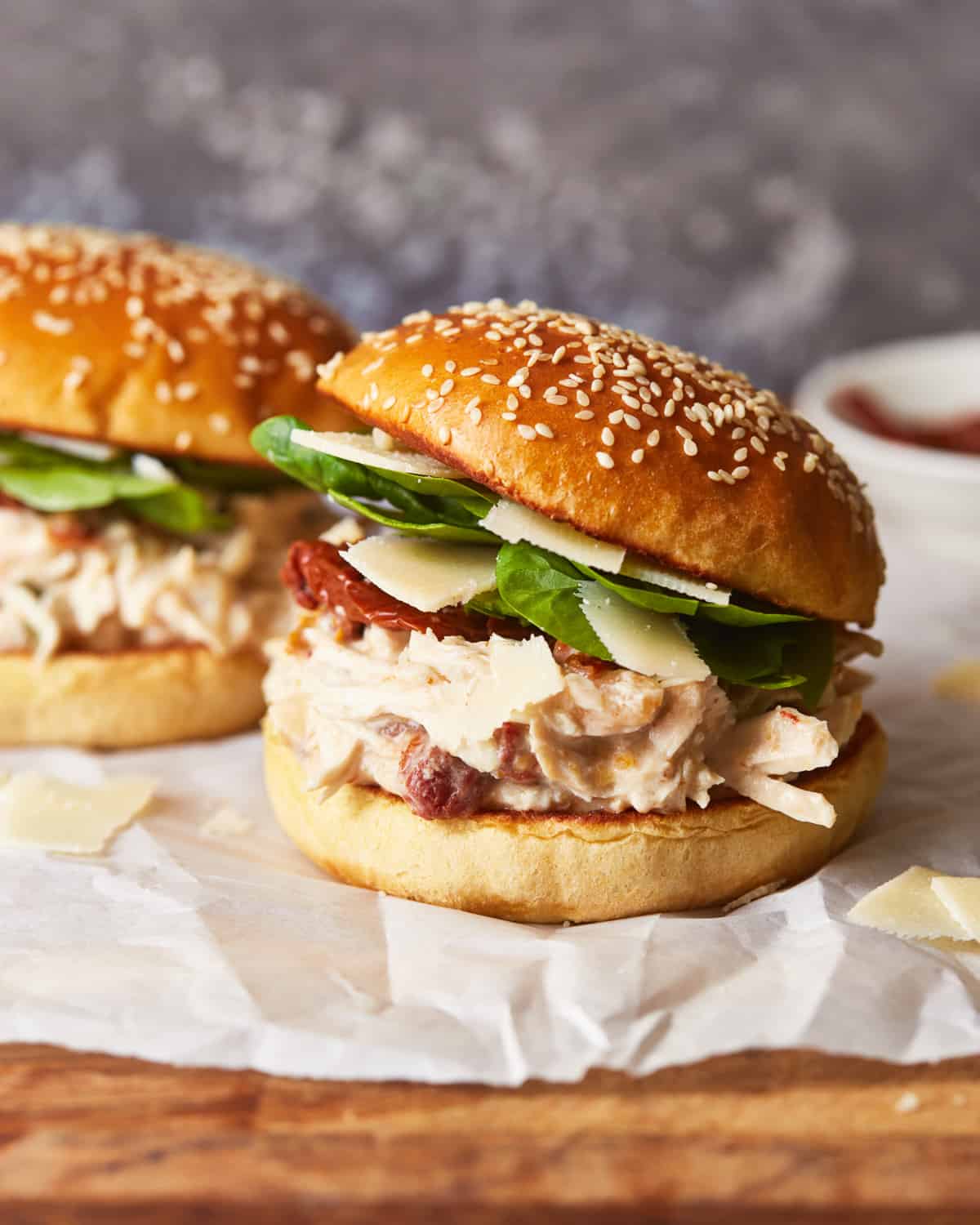 side view of 2 chicken alfredo sandwiches on parchment paper.