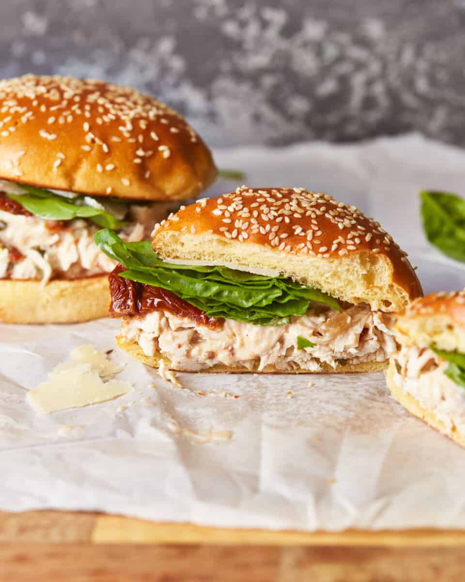 three-quarters view of a halved chicken alfredo sandwich on parchment paper next to a whole sandwich.