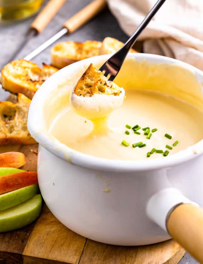 three-quarters view of a piece of grilled bread being dipped into a pot of fondue with a long fork.