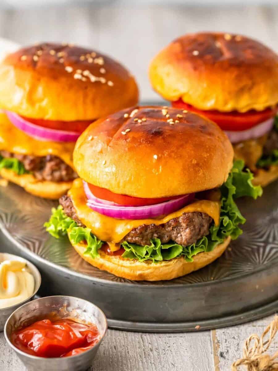 Three hamburgers on a metal plate with ketchup and onions.