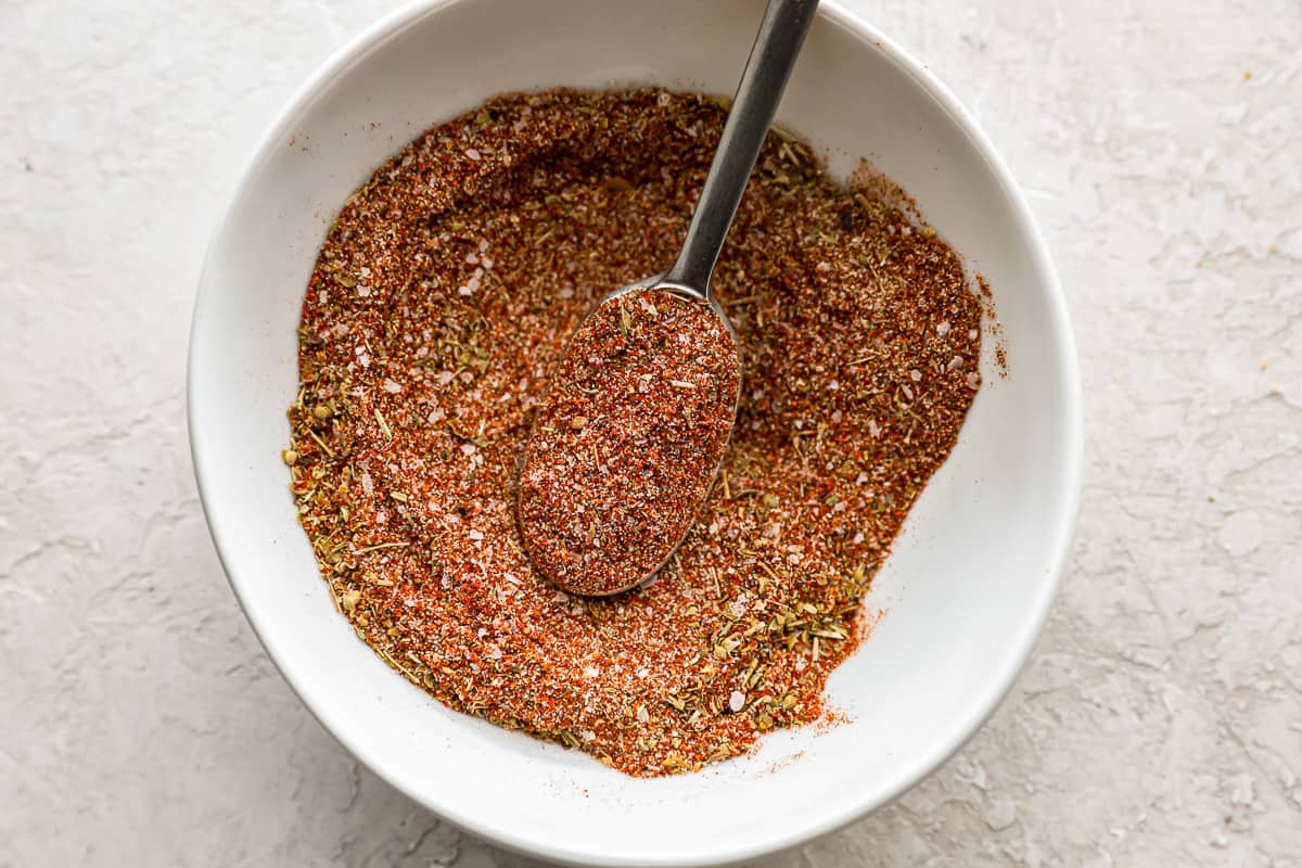 spoon mixing together burger seasoning in a white bowl.