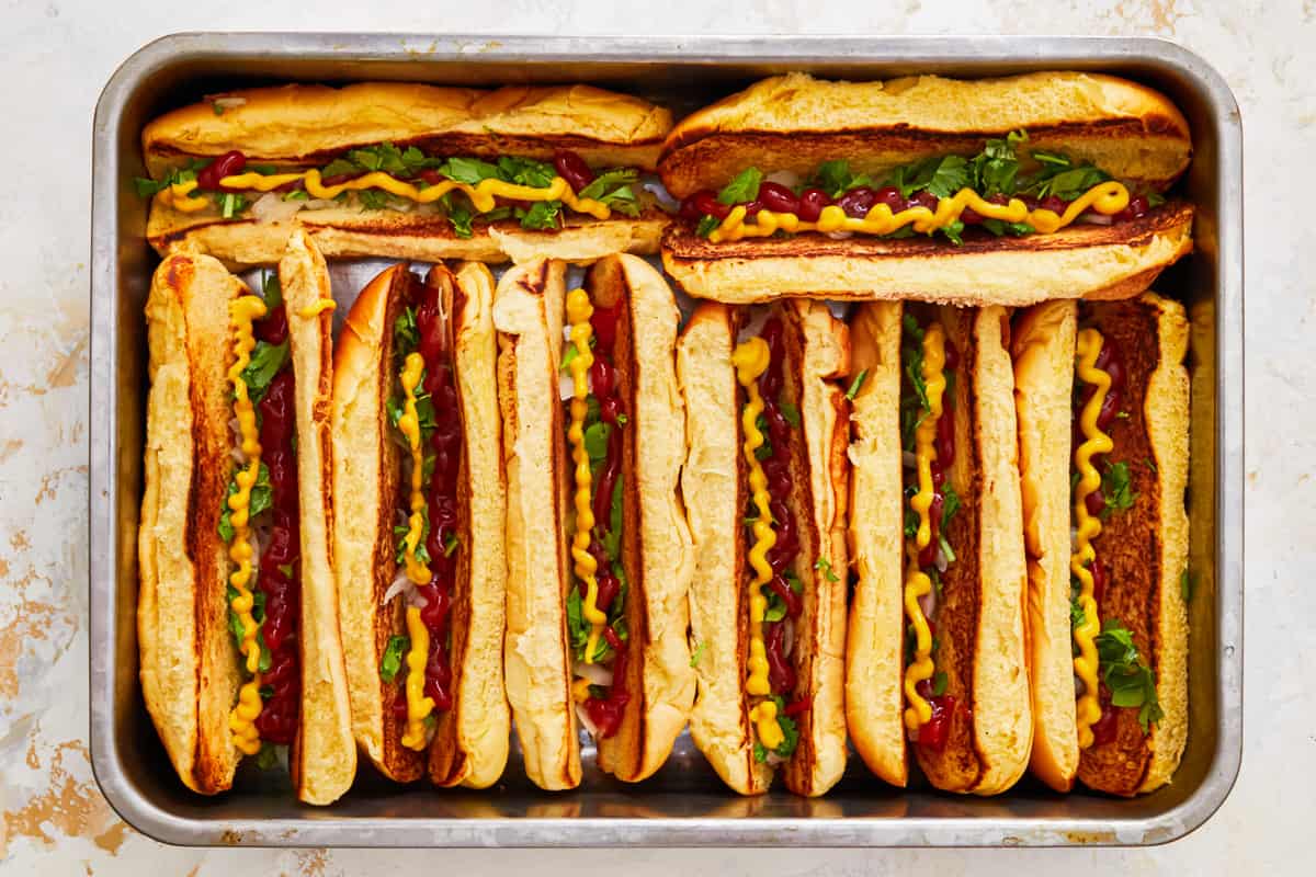 onions, cilantro, ketchup, and mustard in 8 hot dog buns in a baking pan.