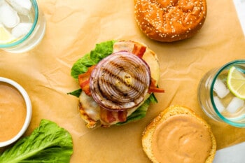 open faced grilled chicken sandwich on parchment paper next to a top bun with sauce slathered on.