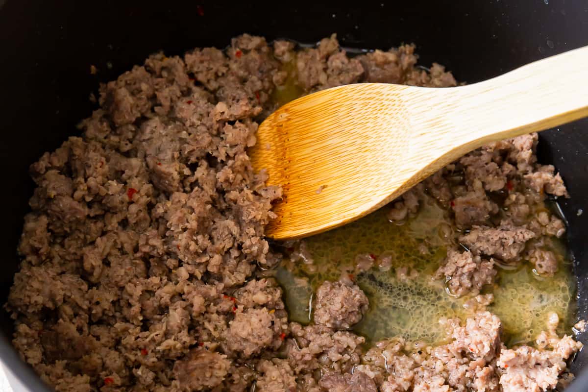 ground sausage cooking in a pot with a wooden spoon.