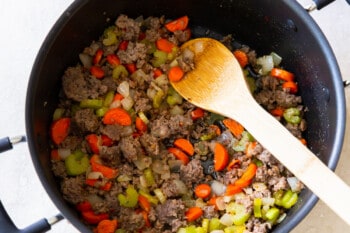 cooked sausage and veggies in a pot with a wooden spoon.