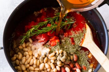 broth added to pasta e fagioli soup in a pot with a wooden spoon.