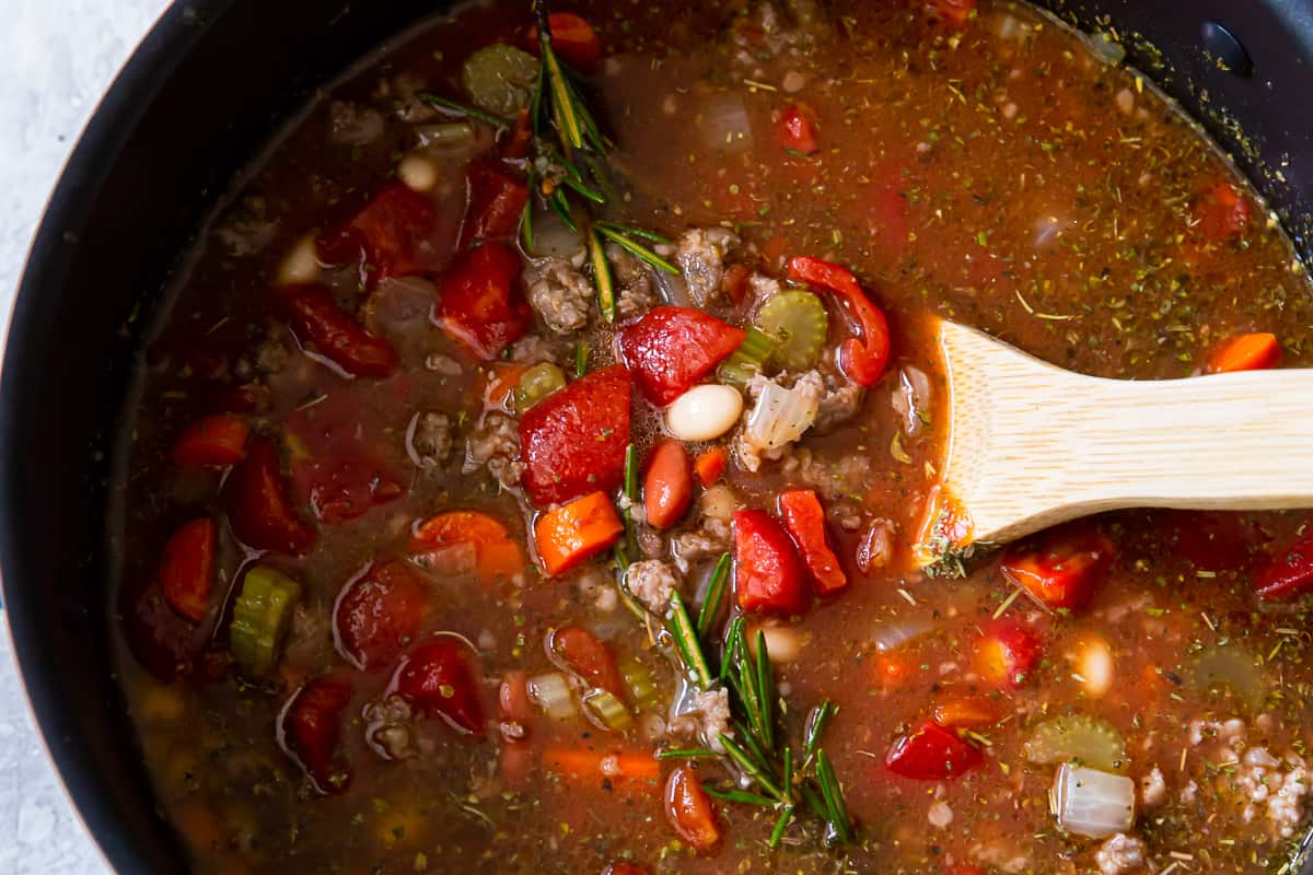 pasta e fagioli soup in a pot with a wooden spoon.