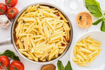 penne pasta in a pan with tomatoes and herbs.