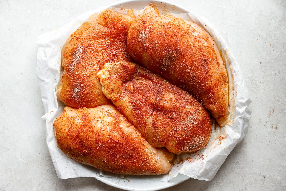 uncooked, seasoned chicken breasts on a plate.