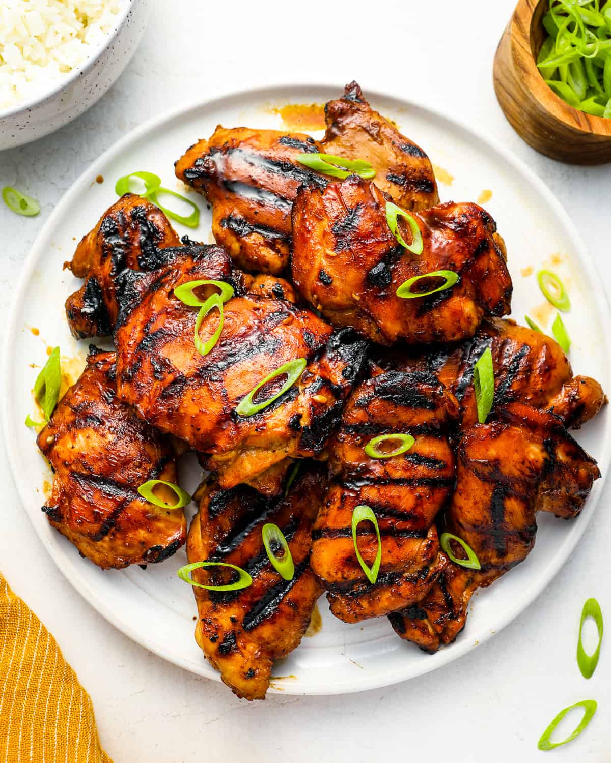 overhead view of grilled huli huli chicken thighs on a white plate topped with green onions.