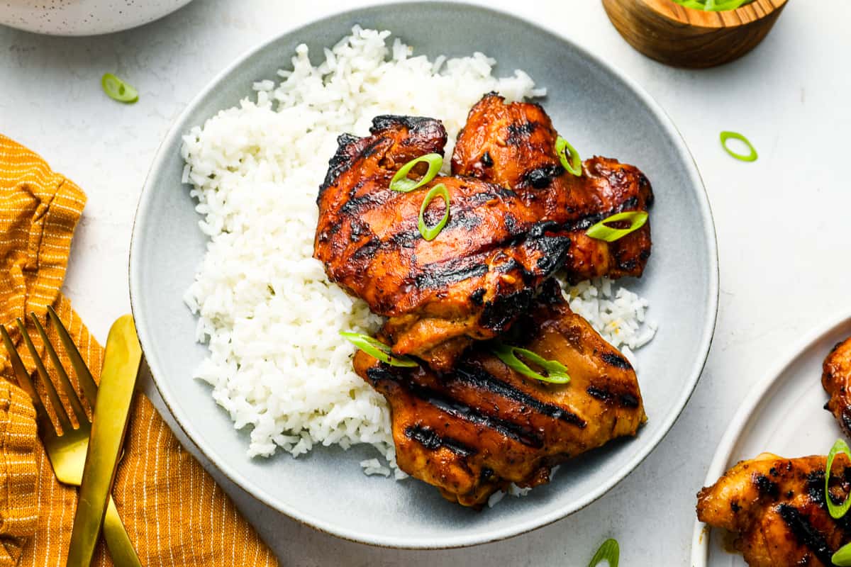 a serving of Hawaiian huli huli chicken on a white plate with rice and green onions.