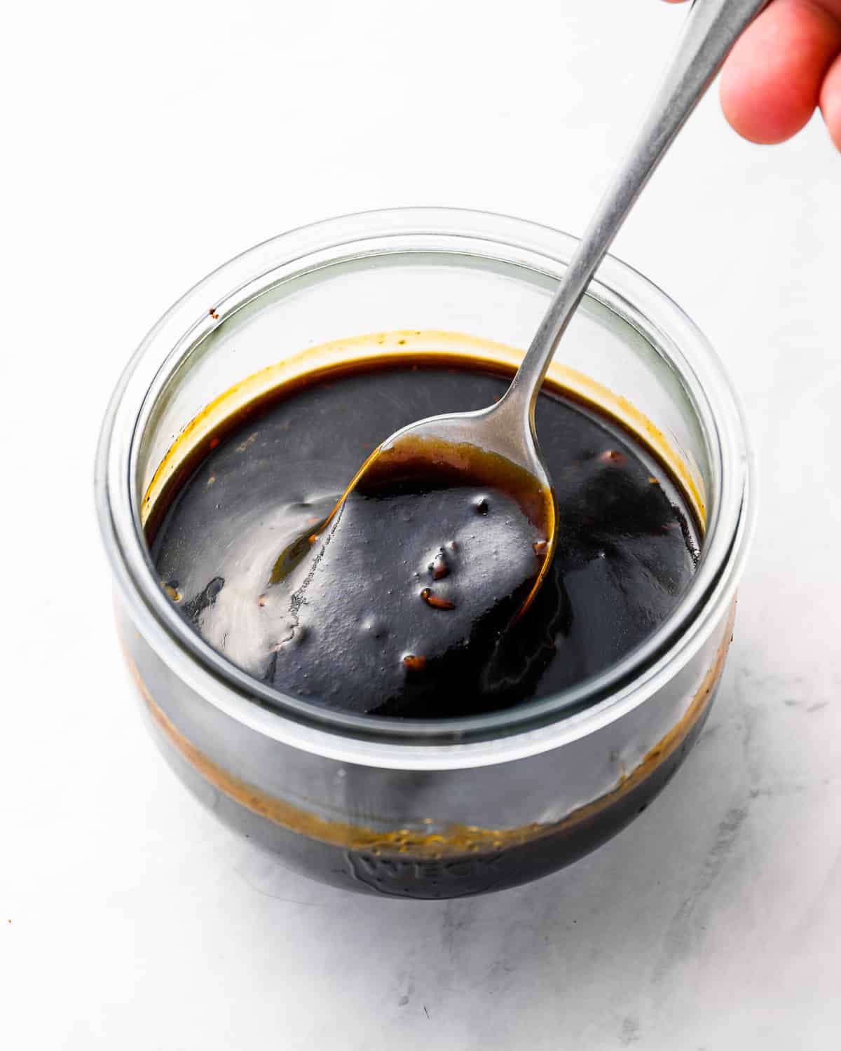 three-quarters view of a spoon stirring korean bbq sauce in a glass bowl.