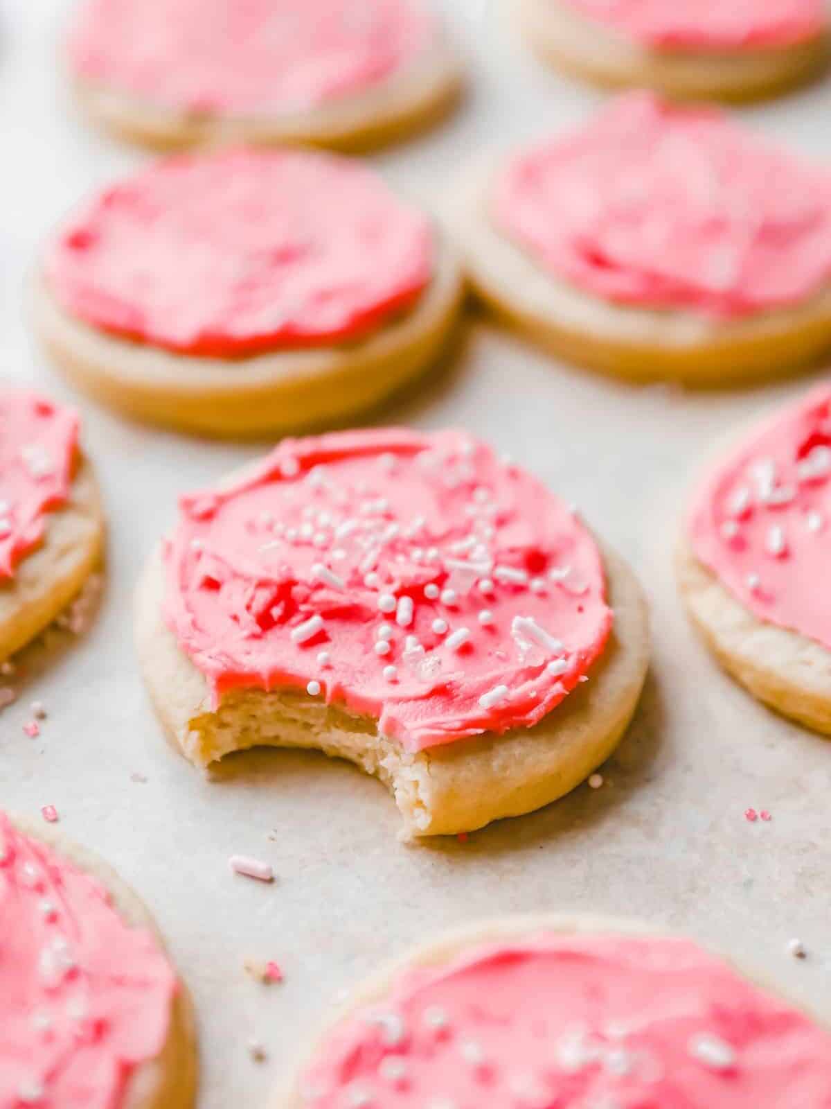 three-quarters view of pink frosted lofthouse cookies on parchment paper, one is bitten.