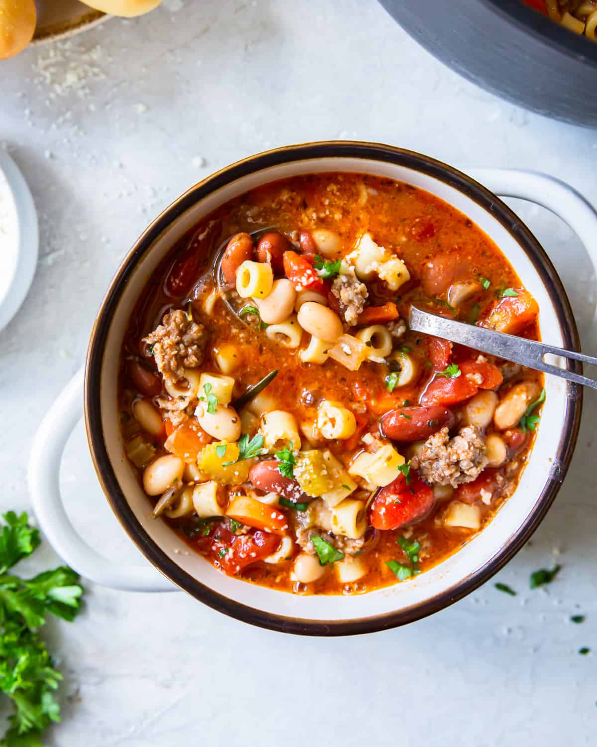 overhead view of a serving of pasta e fagioli soup in a white tureen with a spoon.