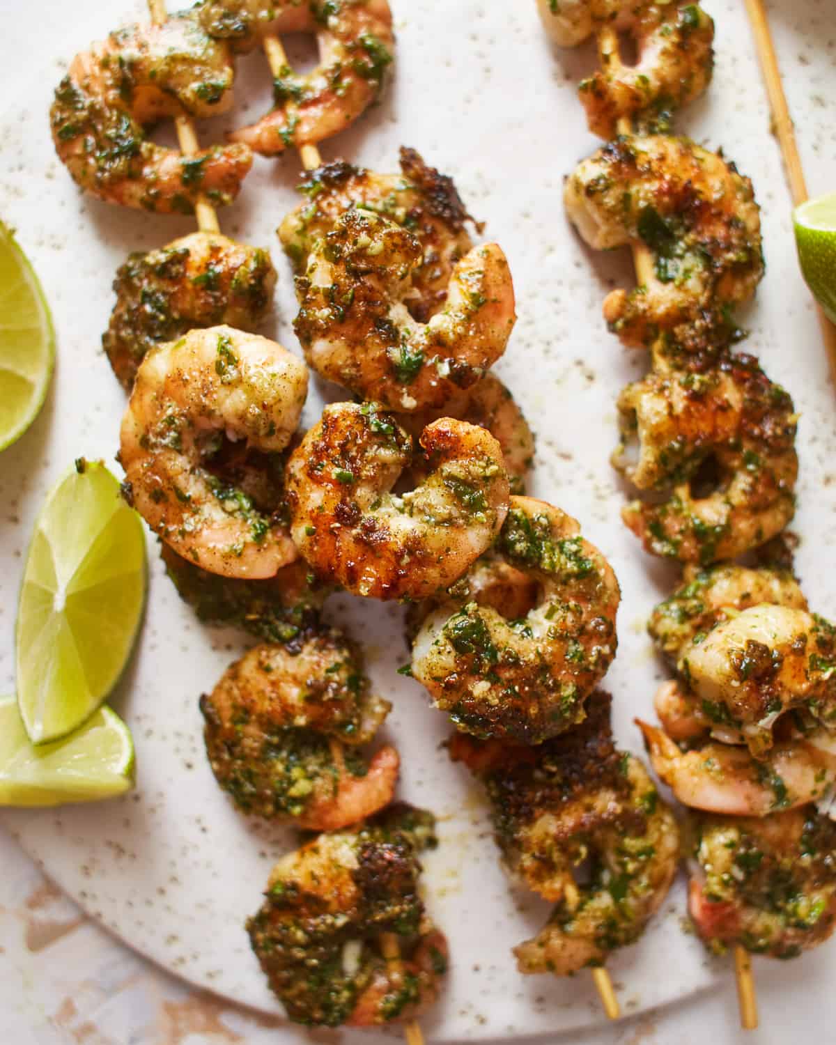 close-up view of 4 pesto shrimp skewers on a white plate.