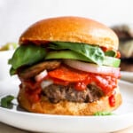 a burger on a plate with tomatoes, lettuce, and other toppings.