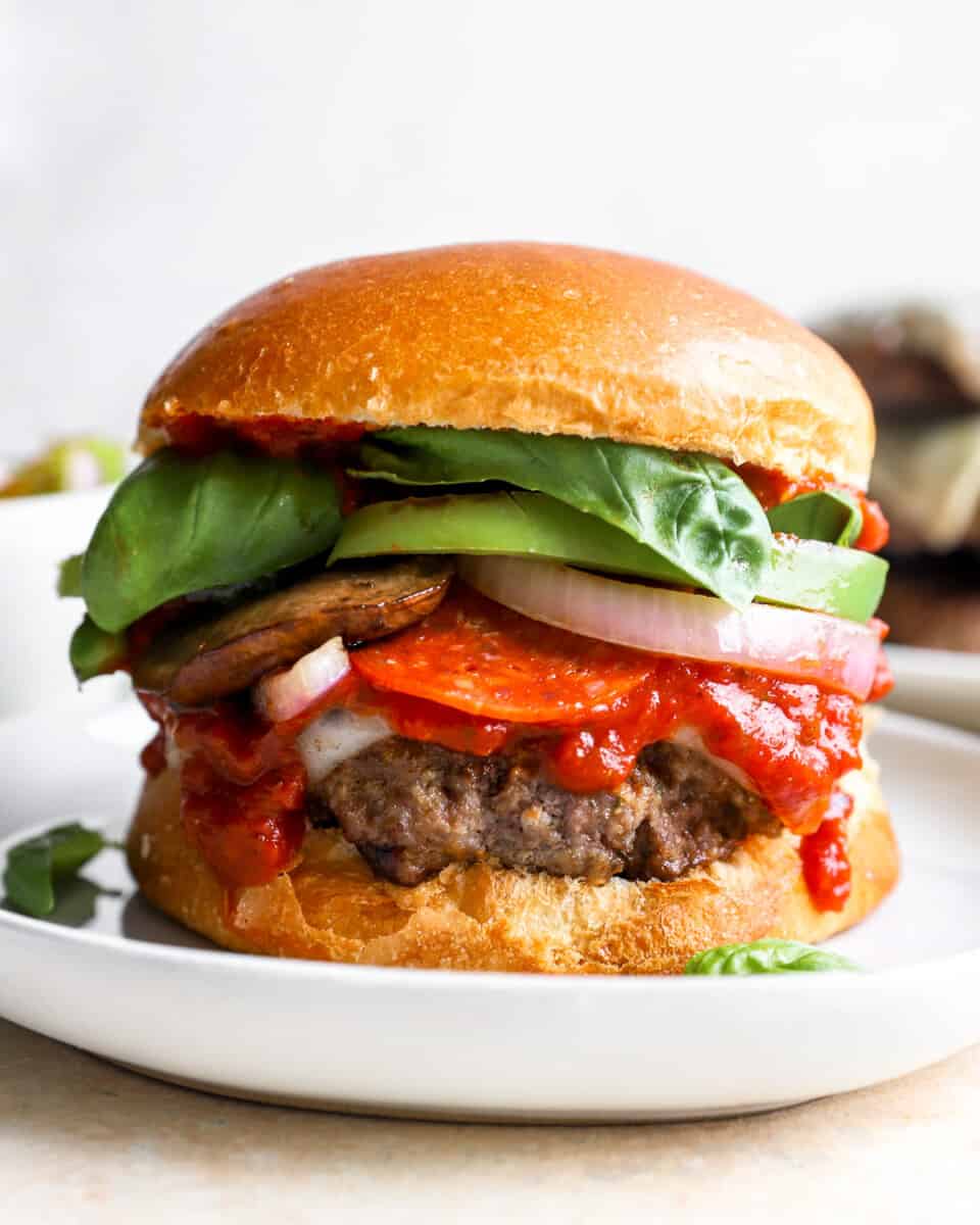 A hamburger topped with pizza sauce, pepperonis, mushrooms, spinach, and onions.