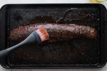 brushing cooked beef tenderloin with butter on a baking sheet.