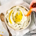 overhead view of a hand dipping a carrot stick into whipped feta dip with olive oil on top.