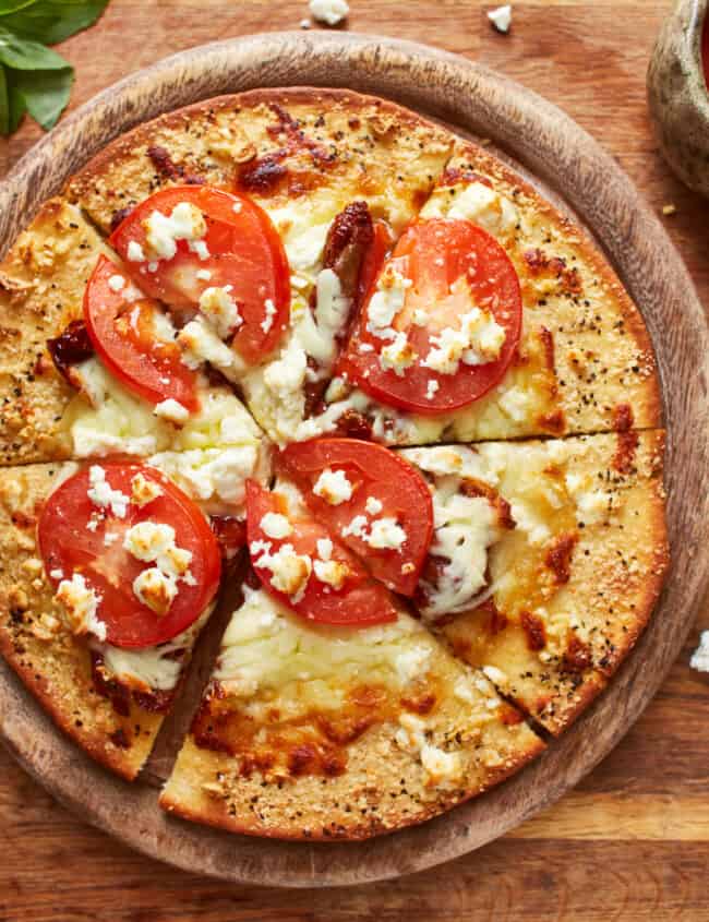 overhead view of a cut white pizza on a round wooden cutting board.