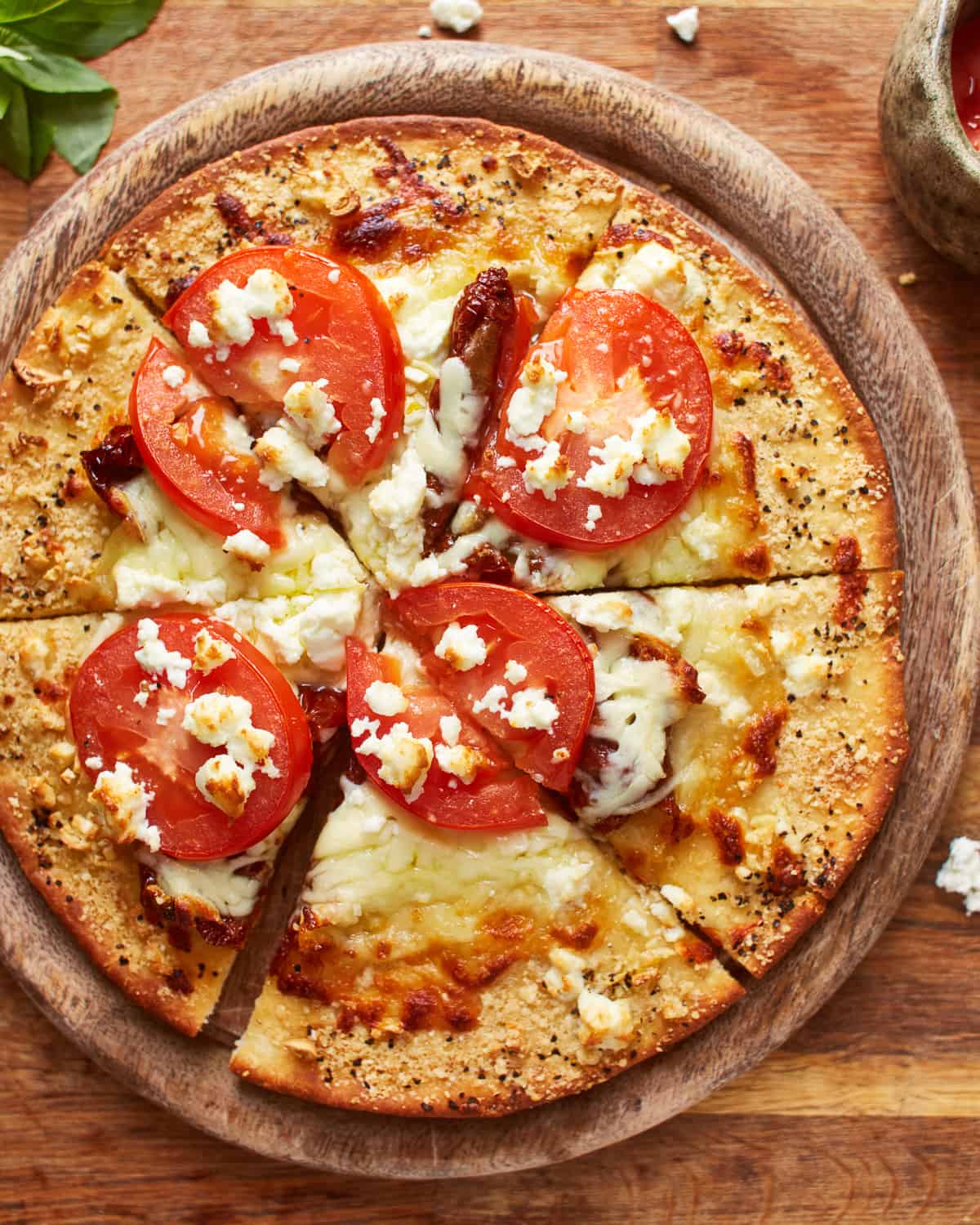 overhead view of a cut white pizza on a round wooden cutting board.