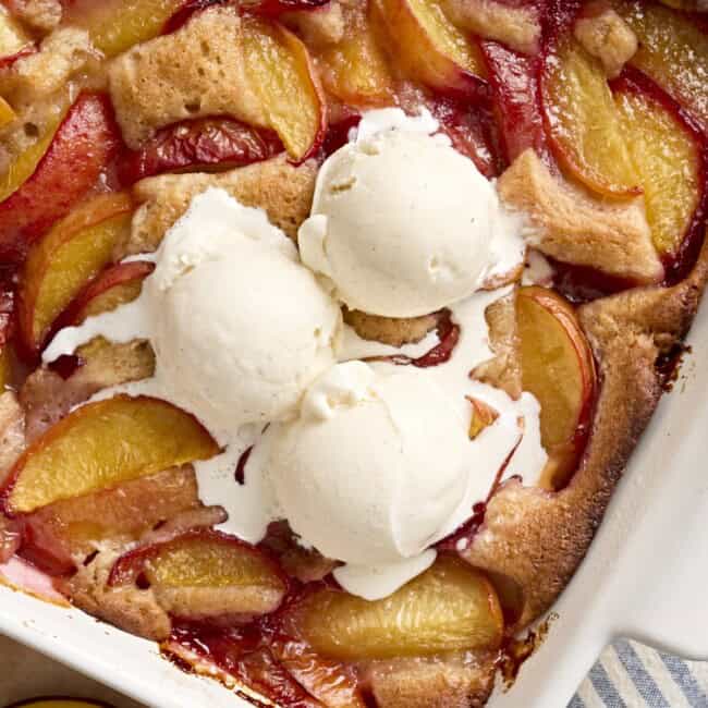 overhead view of scoops of ice cream on peach cobbler in a baking dish.