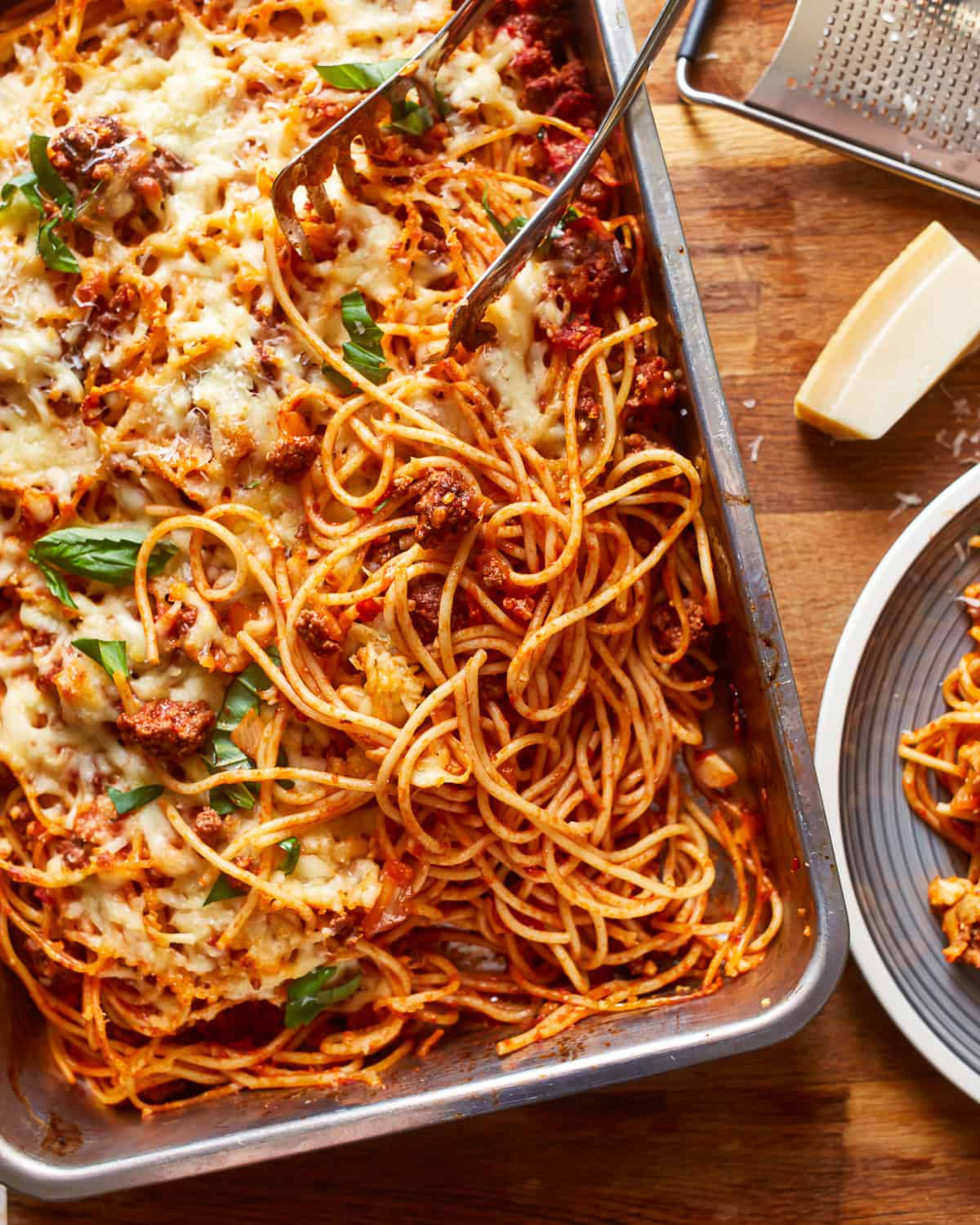 A casserole dish of baked spaghetti with meat sauce, on a wooden table.