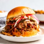 a pulled pork sandwich with coleslaw on a white plate.