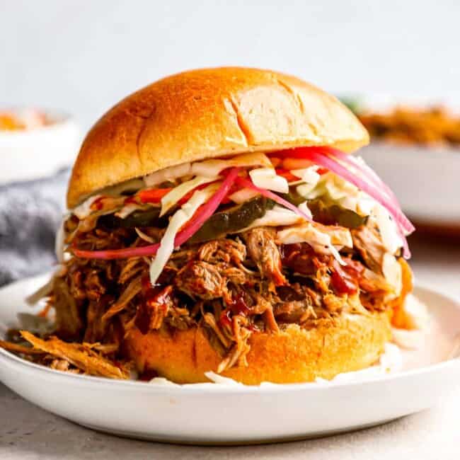 a pulled pork sandwich with coleslaw on a white plate.