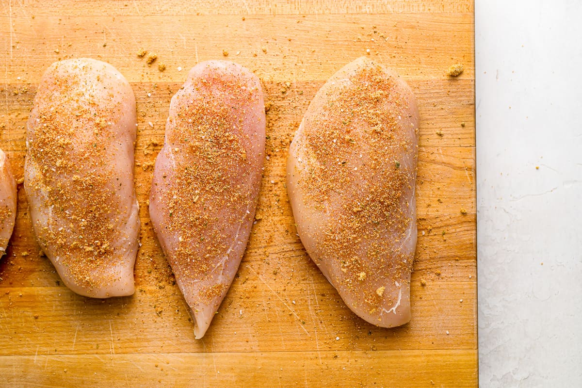 four seasoned chicken breasts on a cutting board.