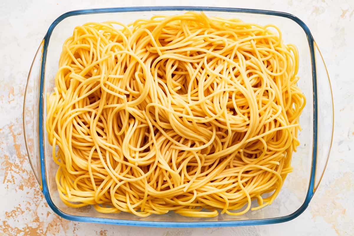 Cooked spaghetti noodles in a glass baking dish,l on a white surface.