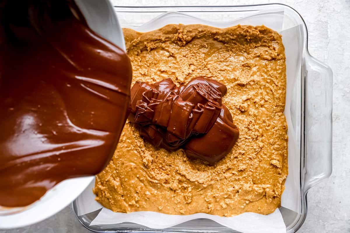 chocolate being poured over a brownie in a baking dish.