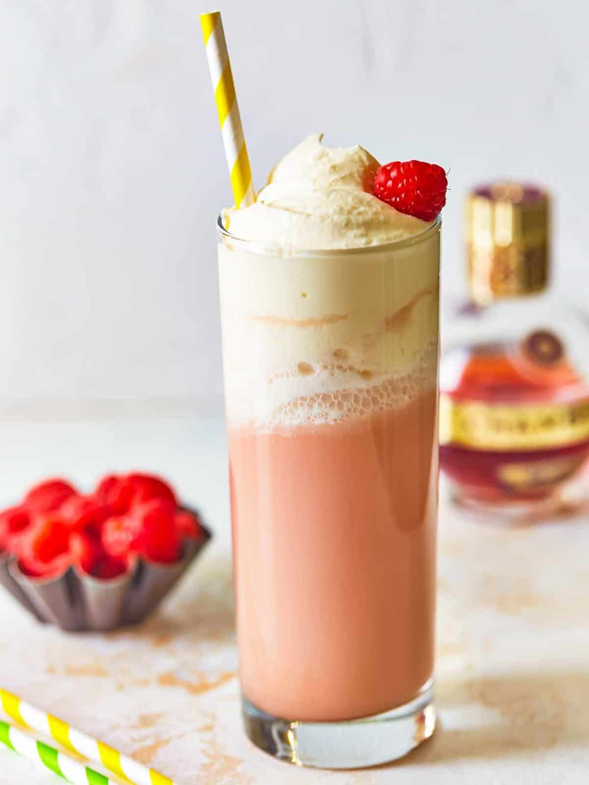 side view of raspberry italian cream soda in a tall glass topped with whipped cream, a raspberry, and a straw.