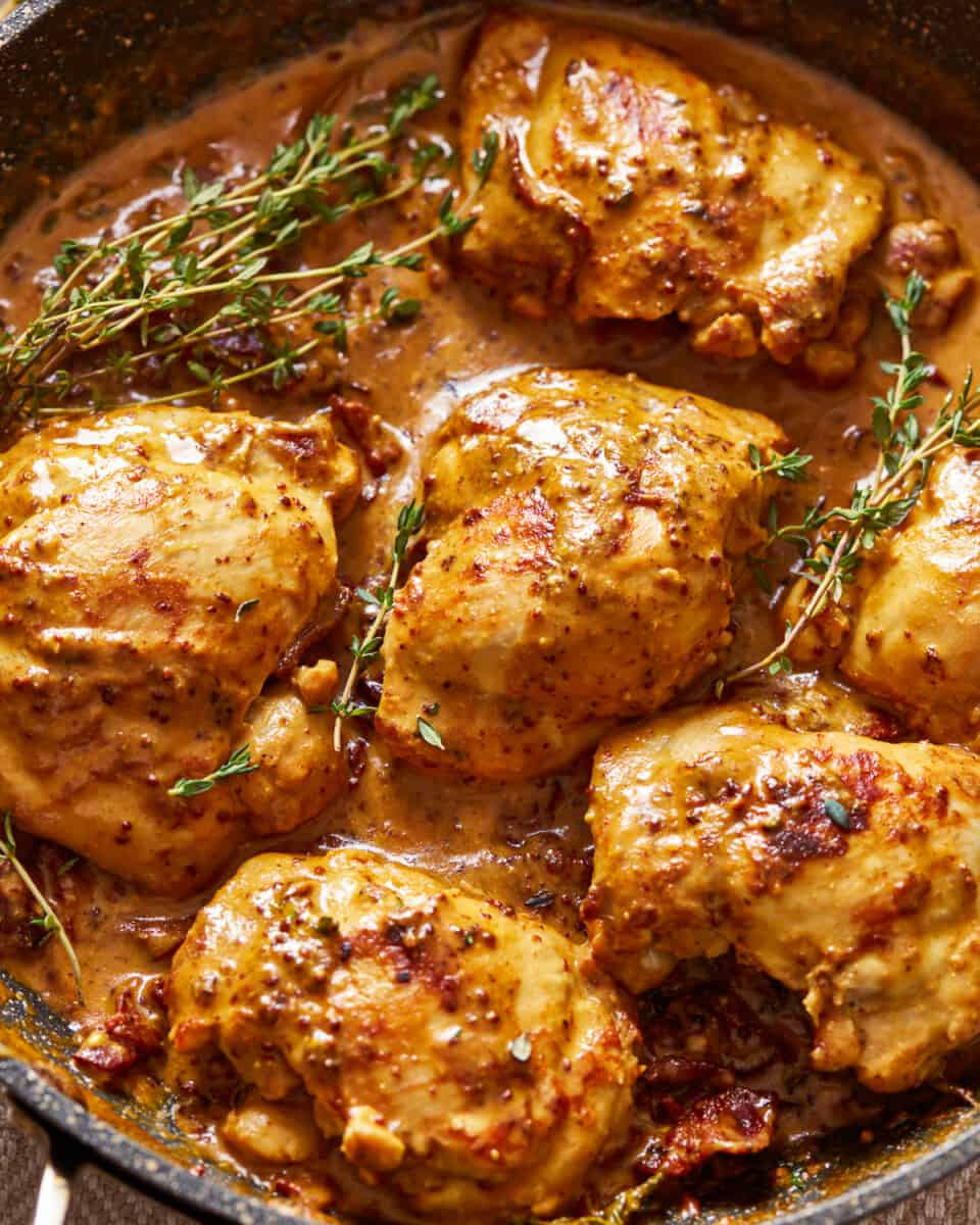 chicken breasts in a skillet with sauce and sprigs of thyme.