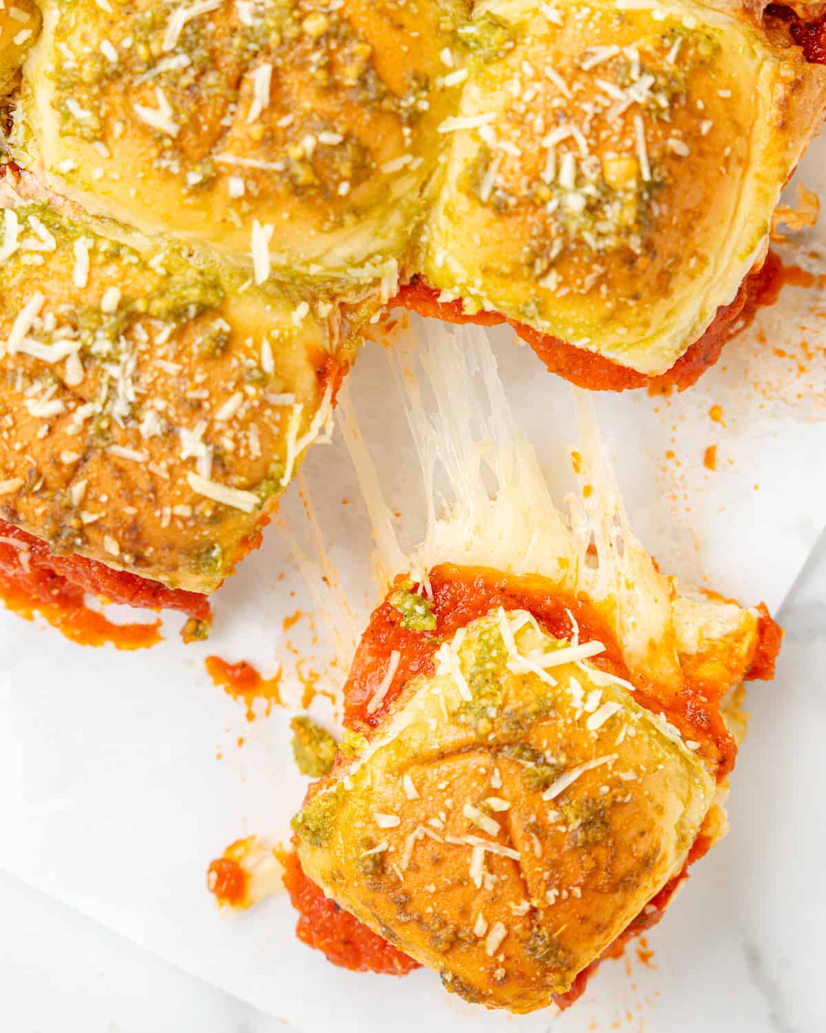 close up on oven-baked sliders with pepperonis, cheese, pesto, and pizza sauce.