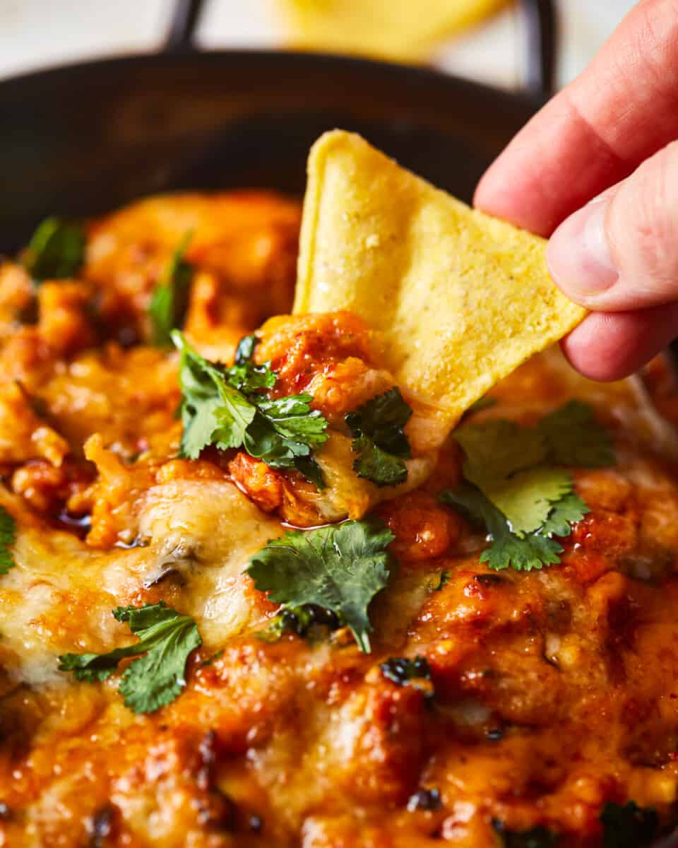 a person dipping a tortilla into a bowl of chicken dip.