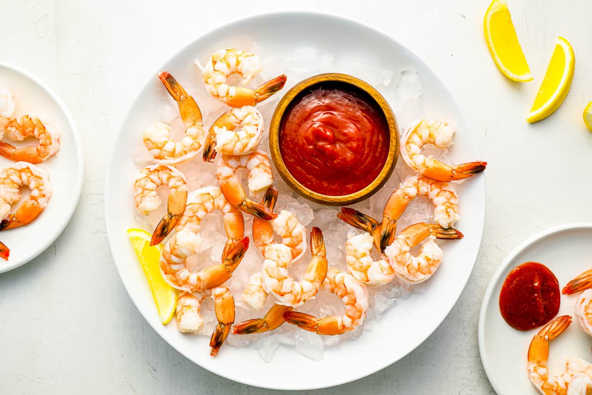 A plate of shrimp cocktail served on ice with lemon wedges.