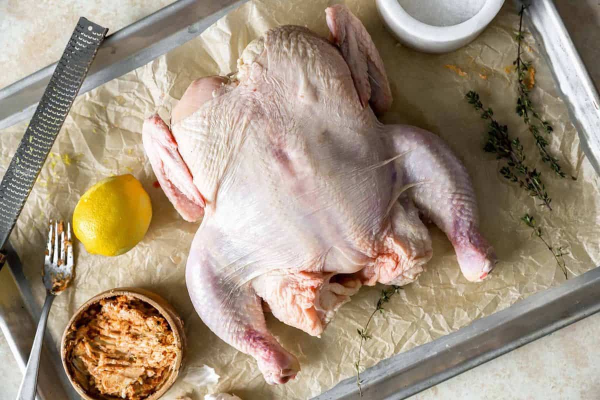 raw spatchcock chicken on a parchment-lined baking sheet surrounded by spice rub ingredients.