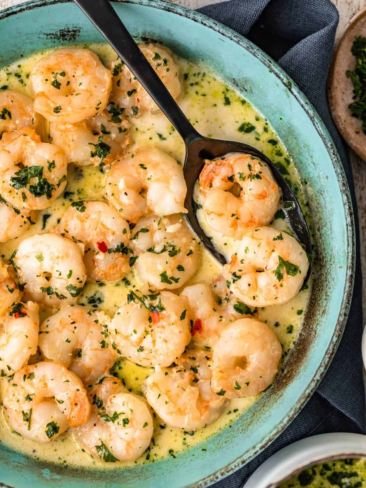 creamy garlic shrimp in a blue bowl with a serving spoon.