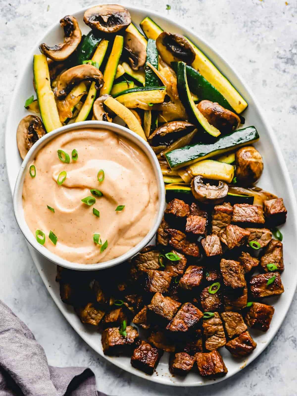 overhead view of homemade yum yum sauce in a white bowl on a platter with cubed steak and vegetables.