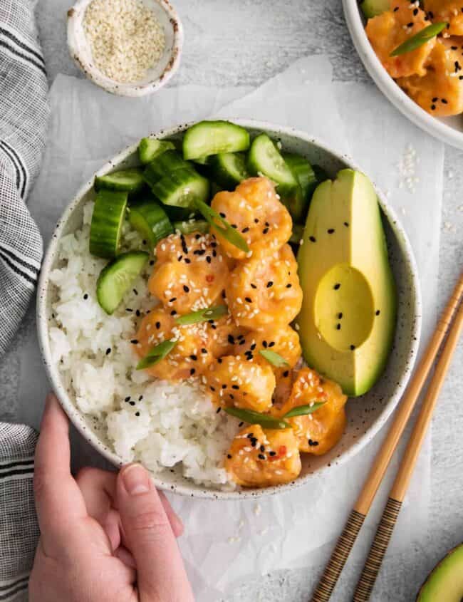 overhead view of a hand grabbing a bang bang shrimp bowl.