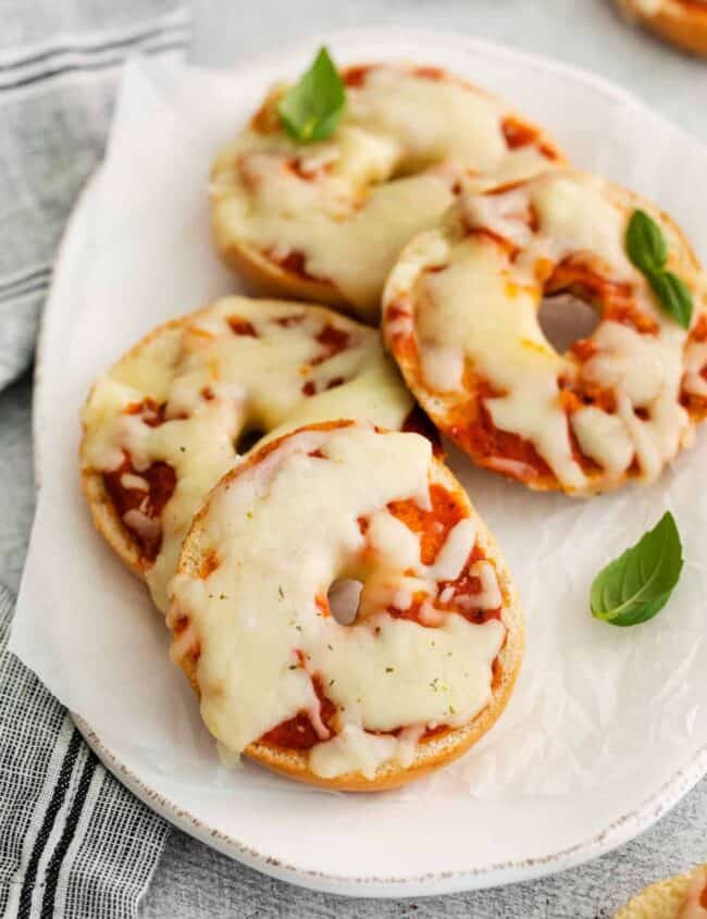 three-quarters view of 4 pizza bagels on an oval serving dish.