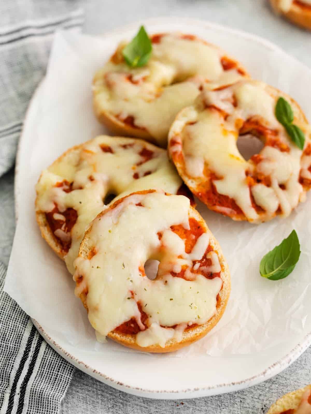 three-quarters view of 4 mini bagel pizzas on an oval serving dish.