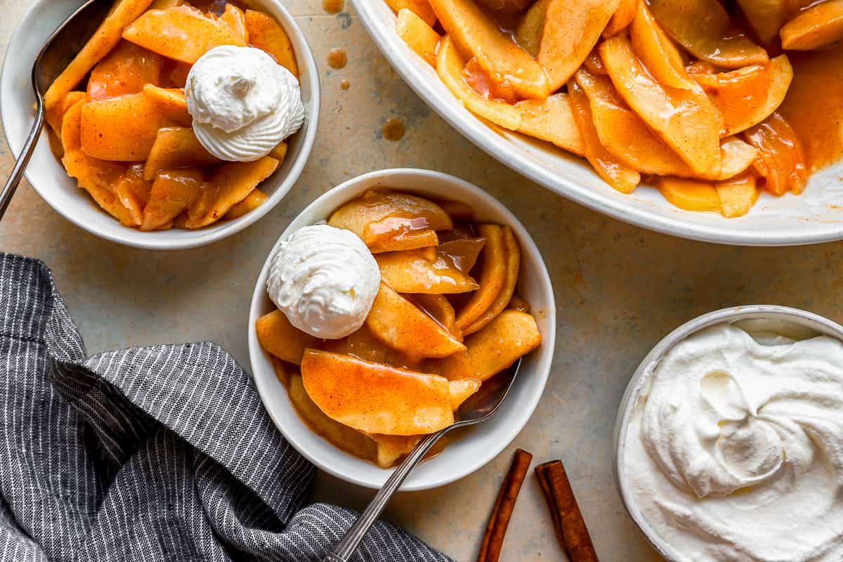 A bowl of warm apple slices with whipped cream and cinnamon.