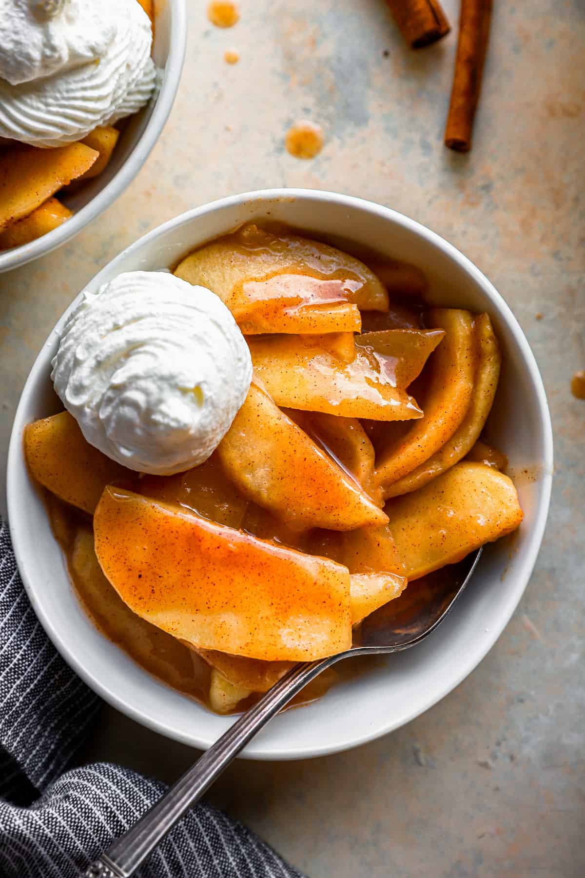 A bowl of baked cinnamon apple with whipped cream and cinnamon sticks.