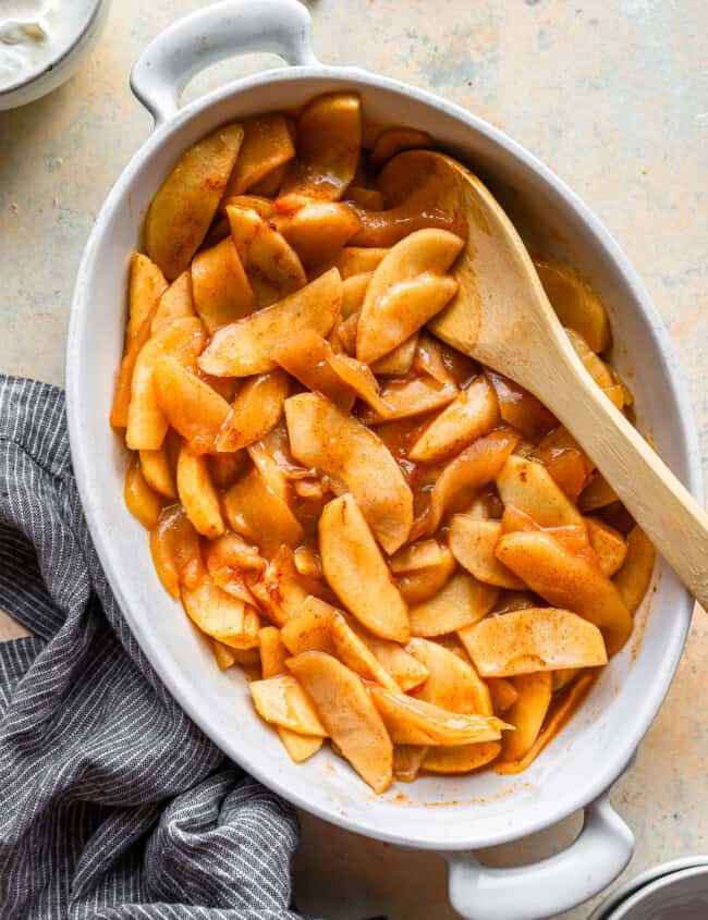 Apples in a dish with a wooden spoon.