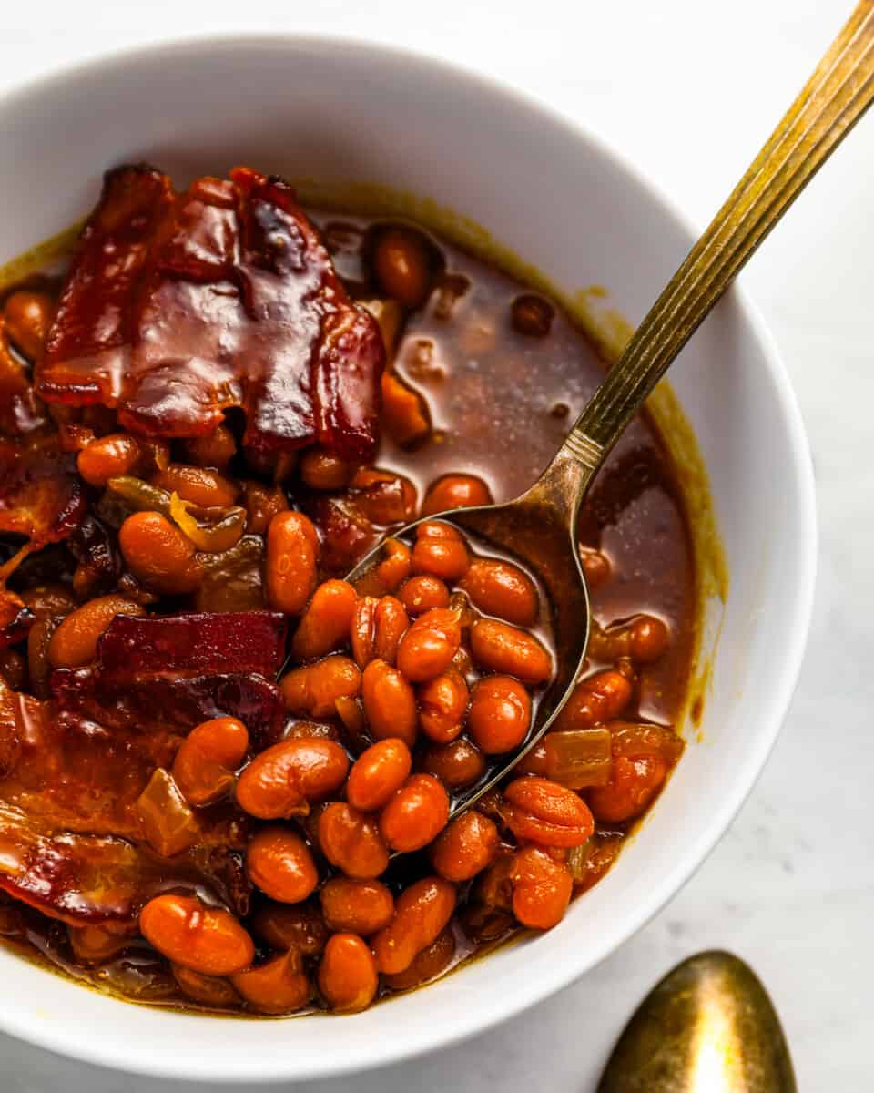 Beans and bacon in a white bowl with a spoon.