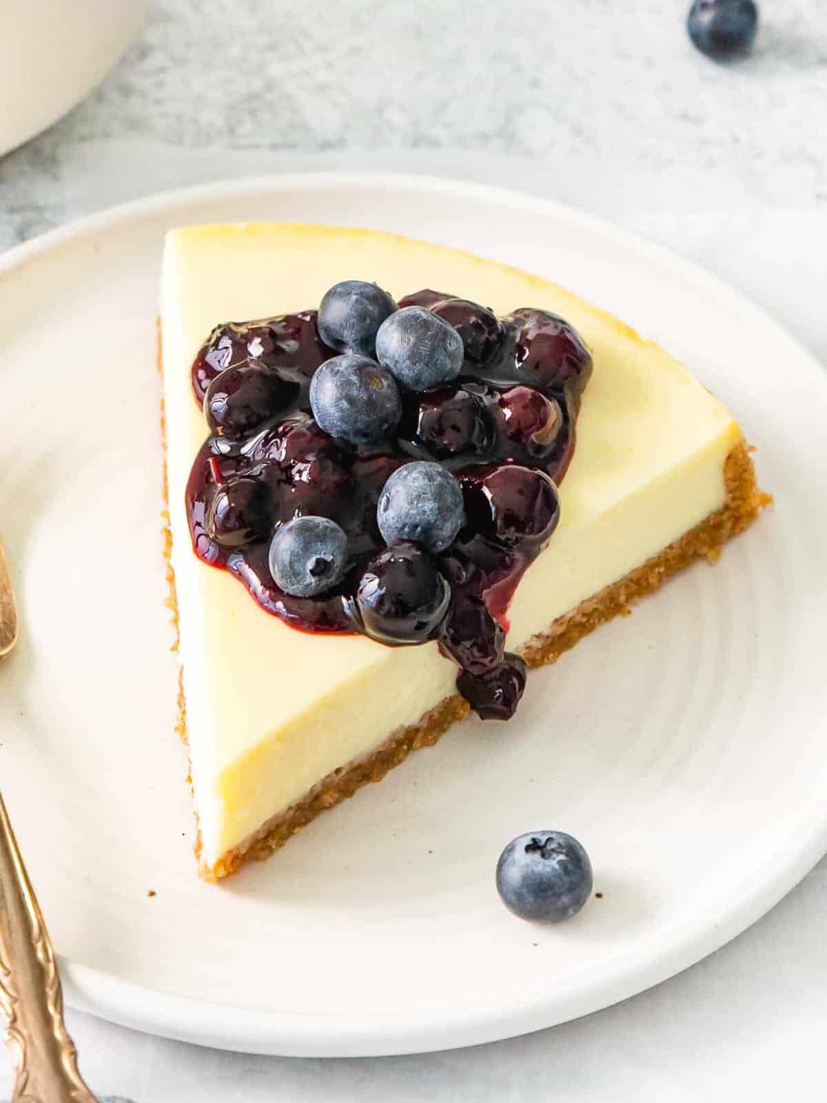 three-quarters view of blueberry compote sauce on top of a slice of cheesecake on a white plate.